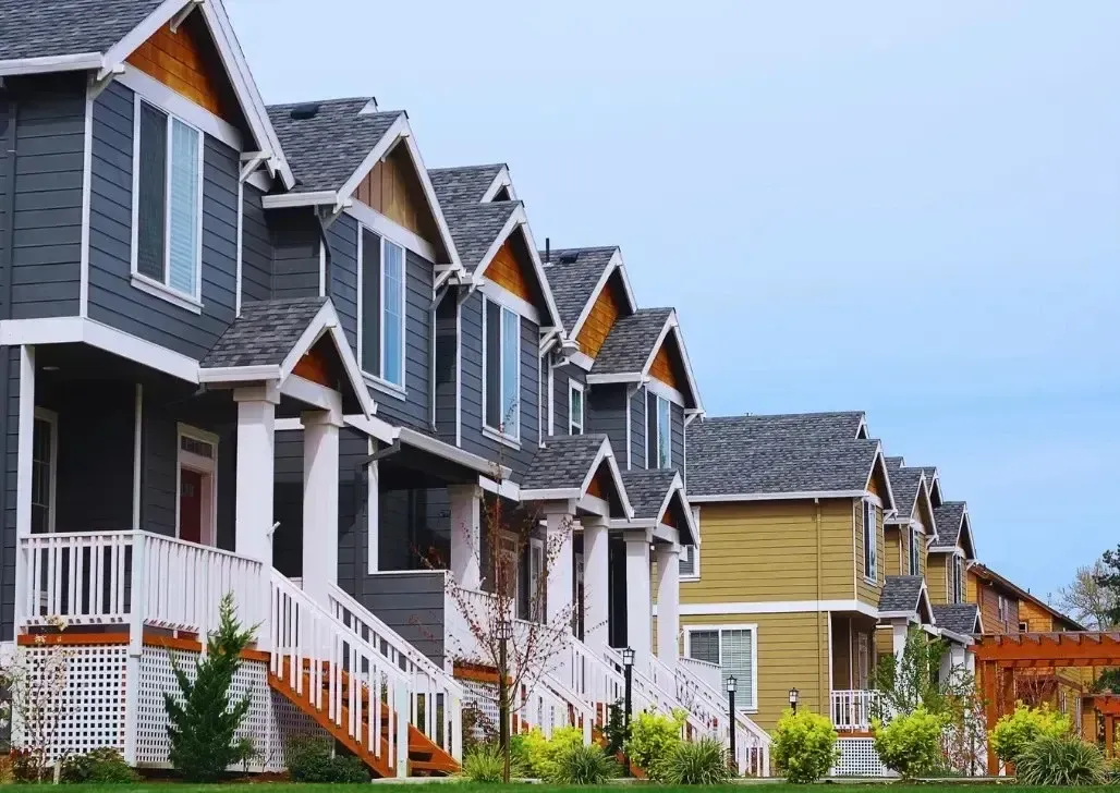Four grayish-blue houses in a charming neighborhood under bright sunlight, with well-maintained lawns and clear skies
