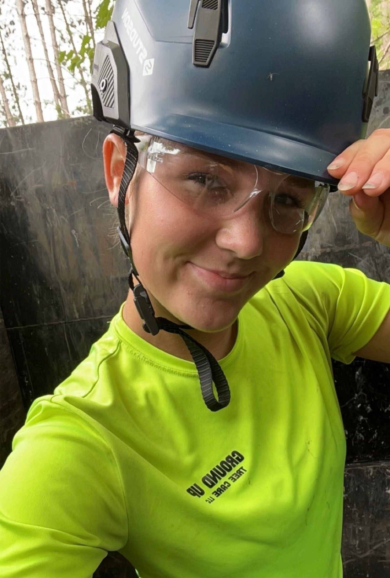 Two people on a lift trimming a tree infected with mistletoe against a cloudy sky.