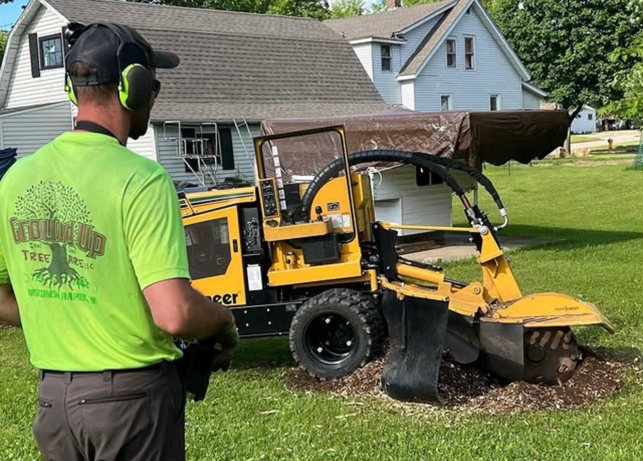 Green stump grinder cutting into a wooden stump, wood chips flying.