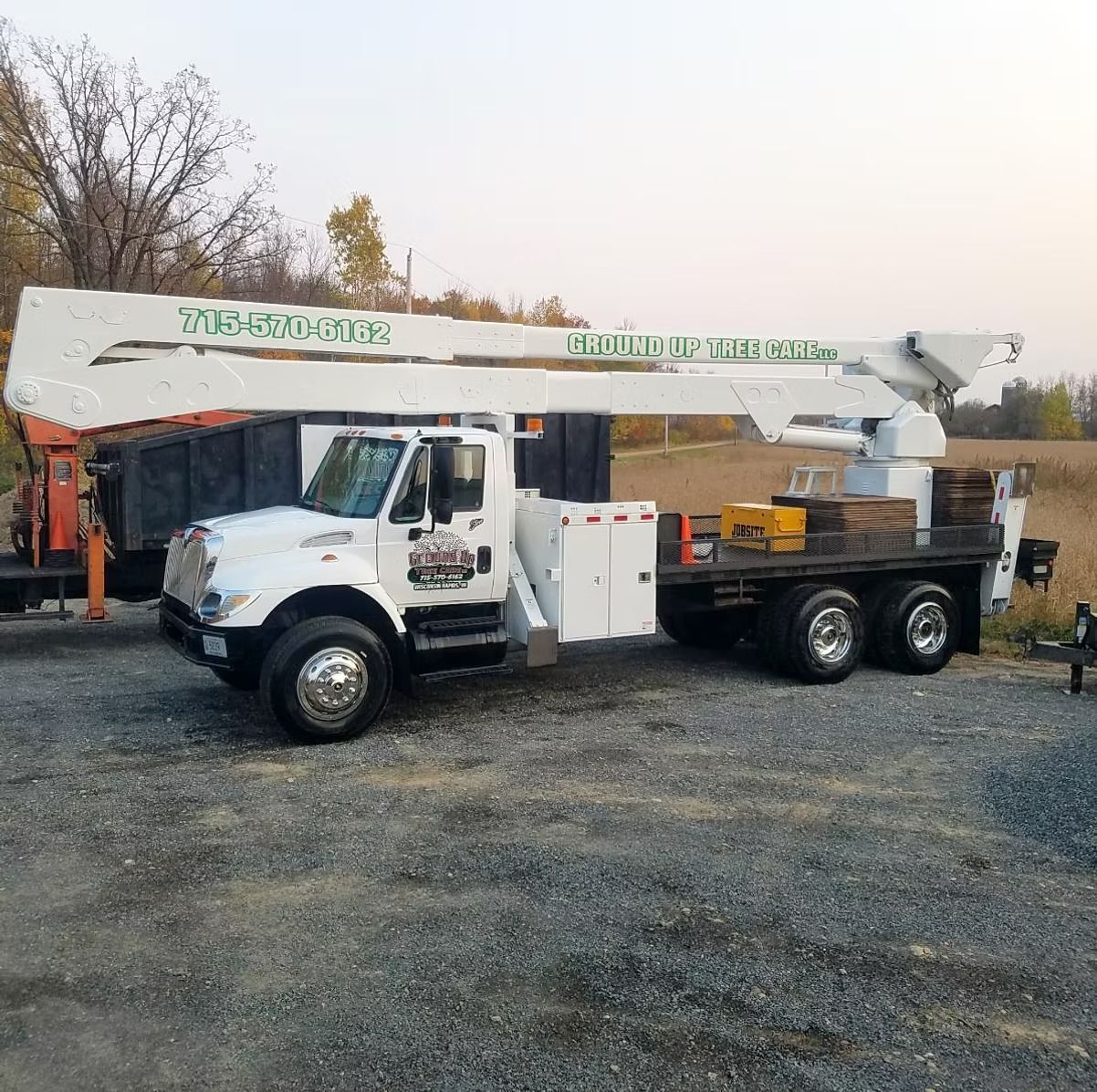 White tree service truck with extended arm, parked on gravel.