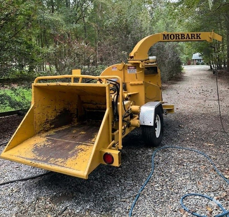 Man feeding brush into orange wood chipper; trailer filled with wood chips.