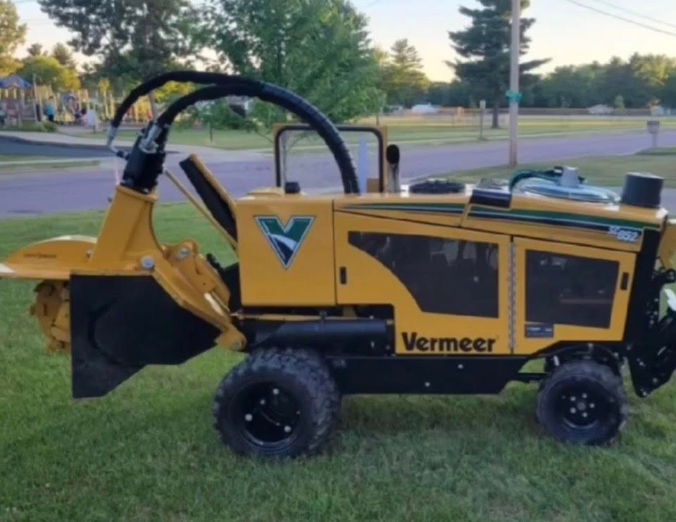 Yellow stump grinder grinding a tree stump in a yard, producing wood chips.