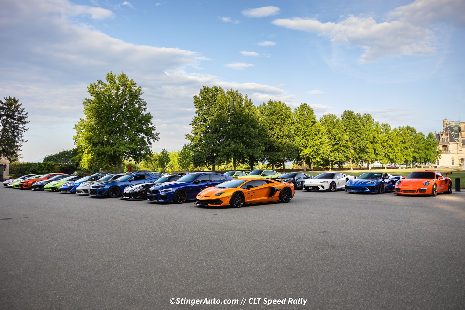 A row of cars are parked in a parking lot with trees in the background