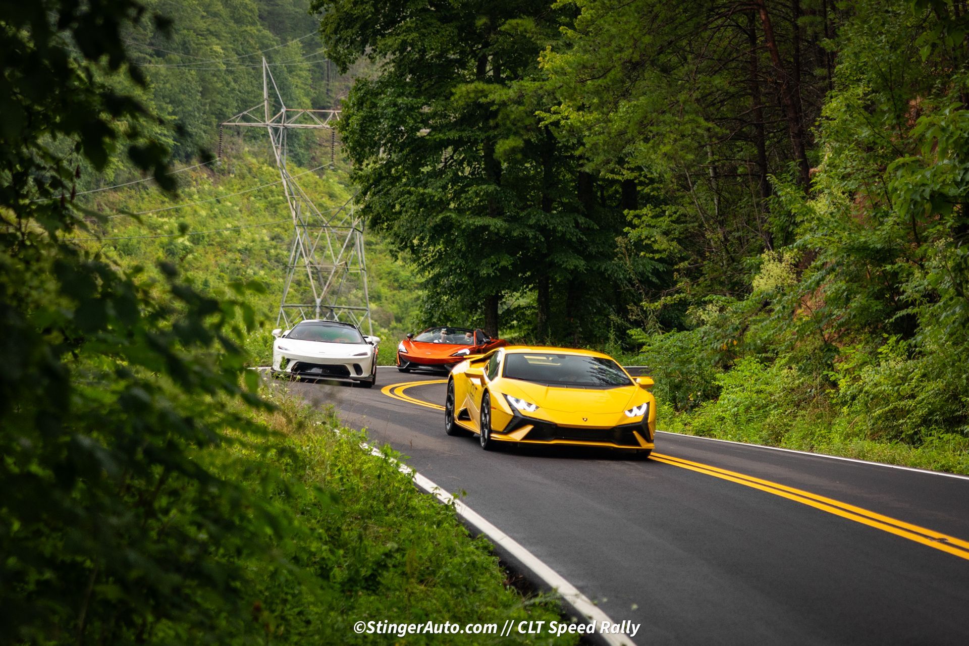 A yellow sports car is driving down a road surrounded by trees