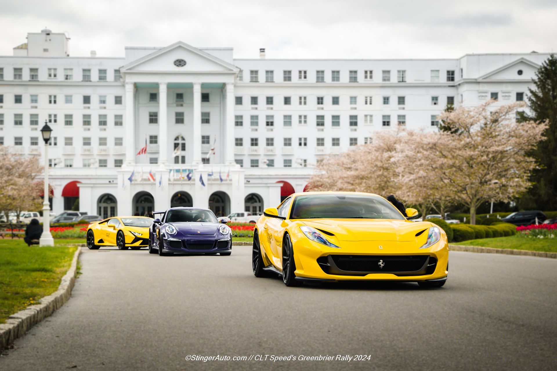 Three cars are driving down a road in front of a large white building