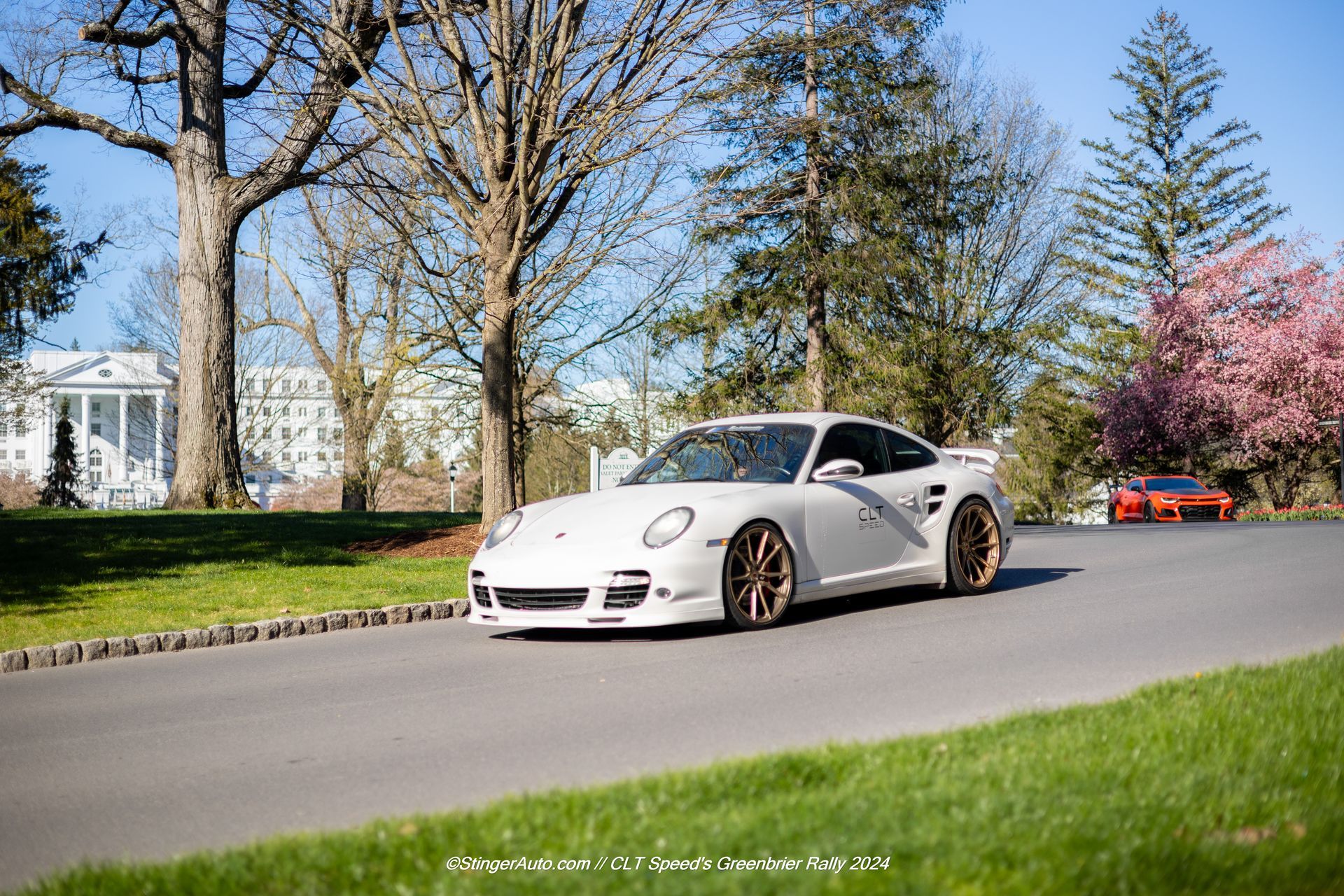 A white sports car is driving down a road surrounded by trees