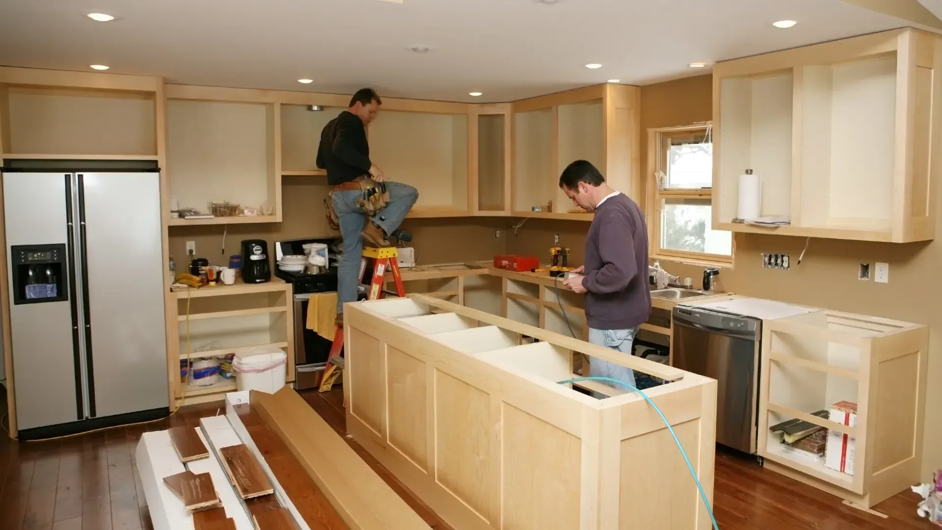 Two men install kitchen cabinets in a newly renovated kitchen.