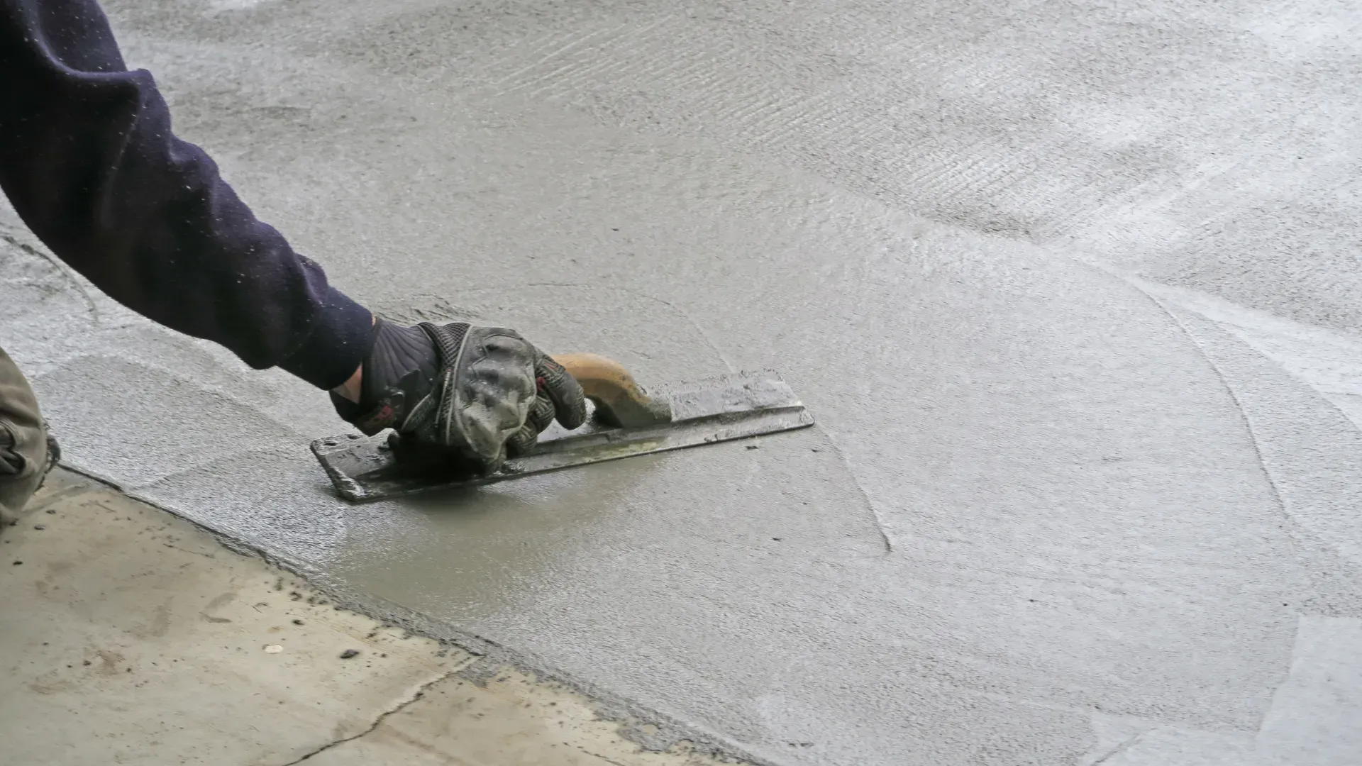 Person smoothing fresh concrete with a trowel outdoors.