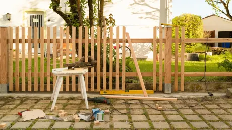 Fence under construction with tools and materials in a sunny yard.