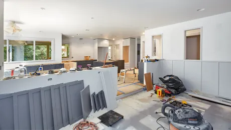 Kitchen under renovation, tools and materials scattered, gray cabinets, white walls.