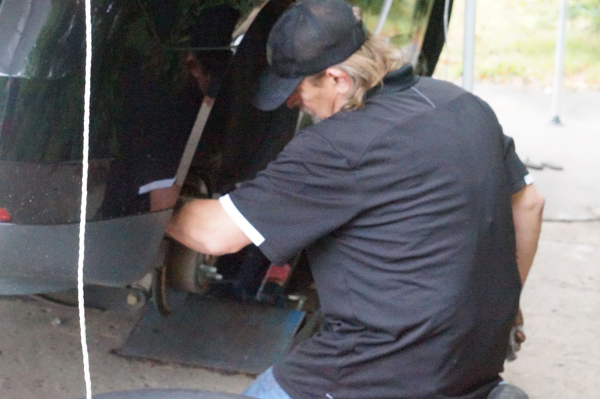 Man in black shirt and hat working on a car's wheel.