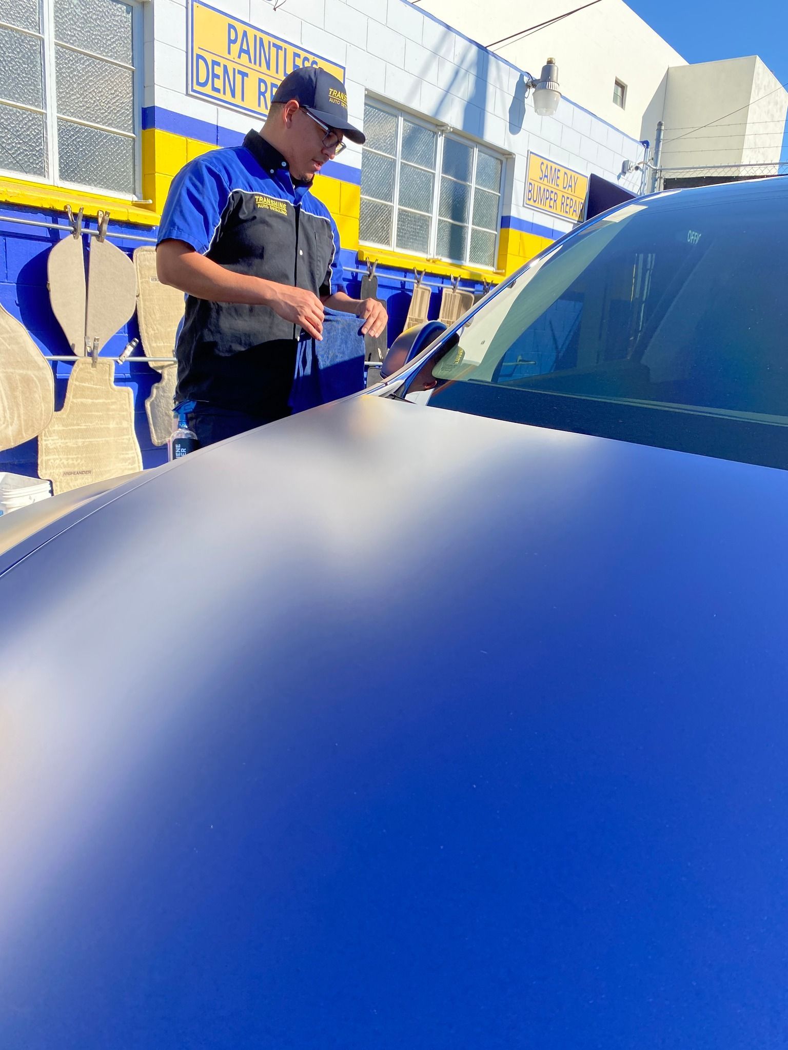 A man is standing next to a blue car in front of a building.