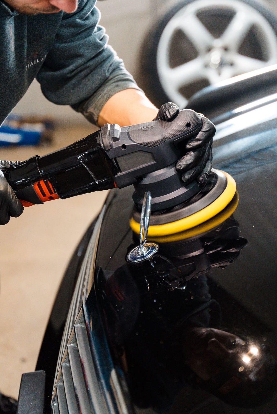 A man is polishing a black car with a machine.