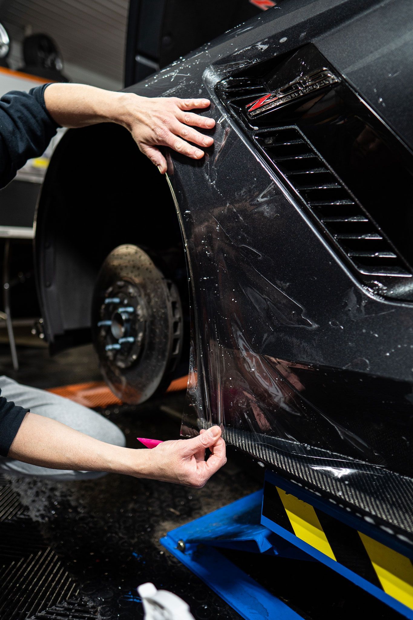 A man is applying a protective film to the side of a car.