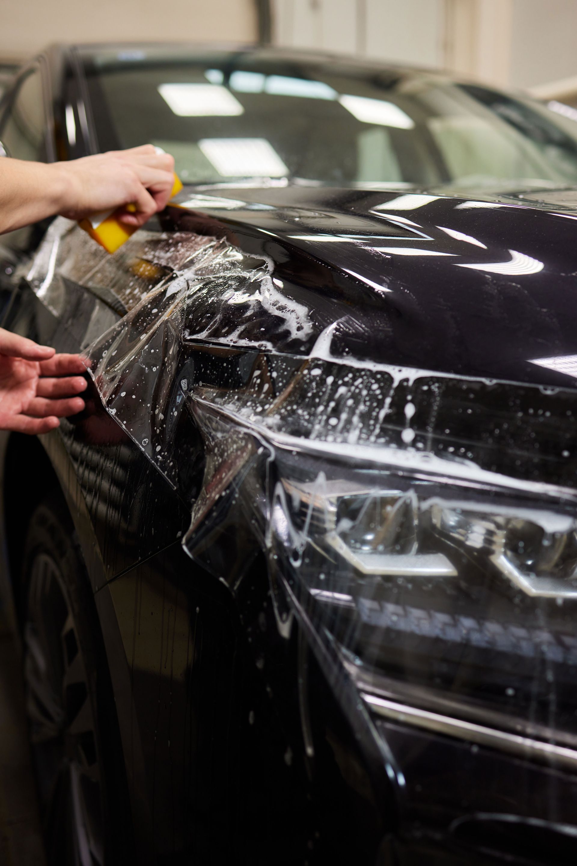 A person is applying a protective film to the hood of a car.