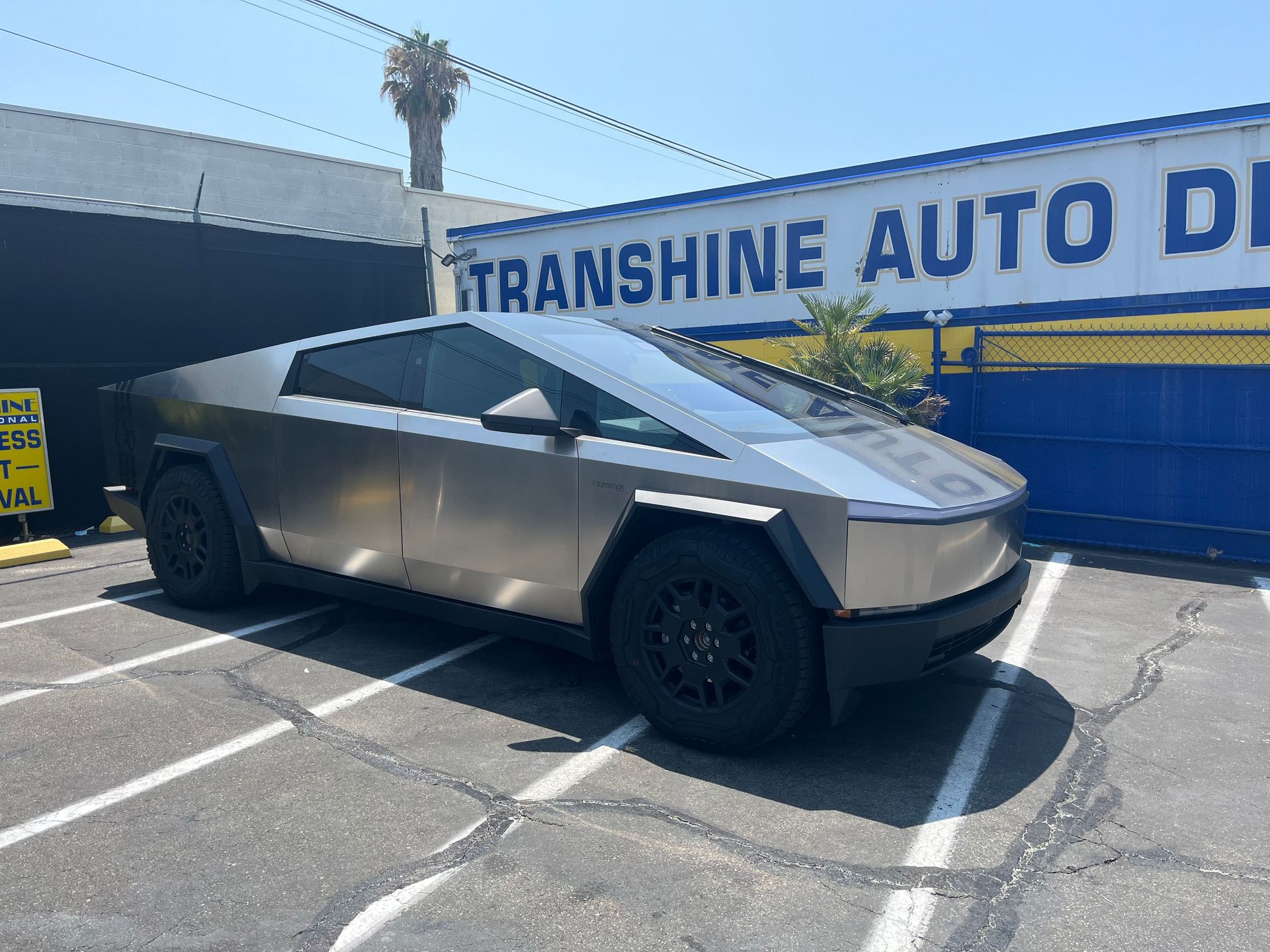 A silver tesla cybertruck is parked in a parking lot in front of a transfine auto detailer.