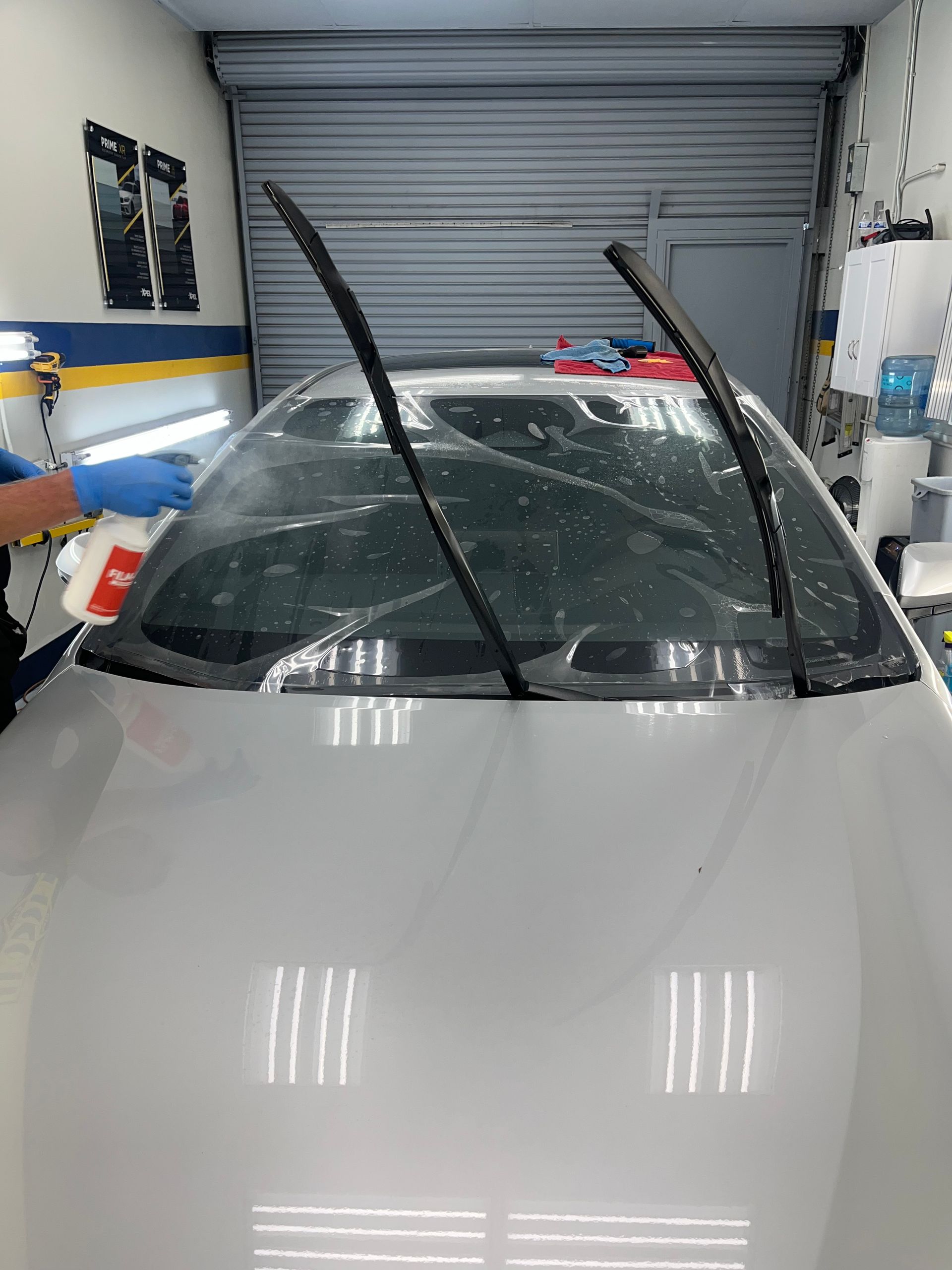 Car being detailed; windshield wipers up, soapy spray on glass. Inside a garage setting.