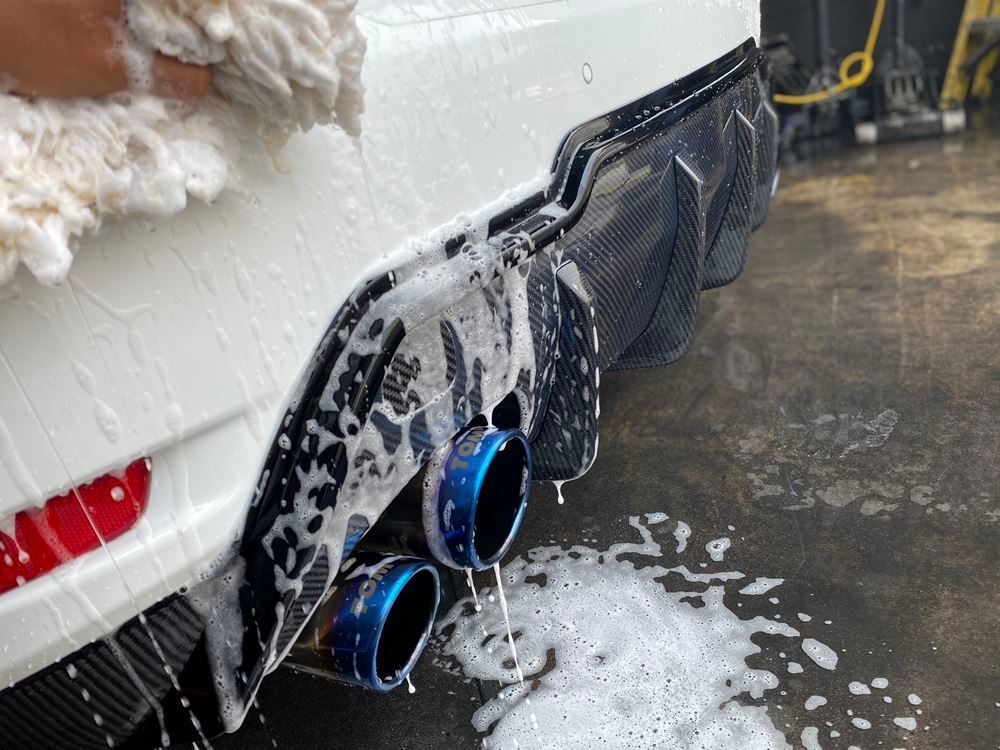 A person is washing a white car with soap and water.