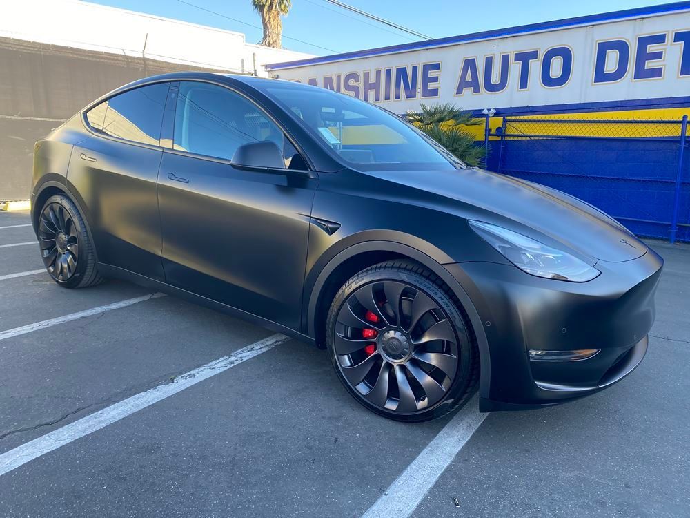 A black tesla model y is parked in a parking lot.