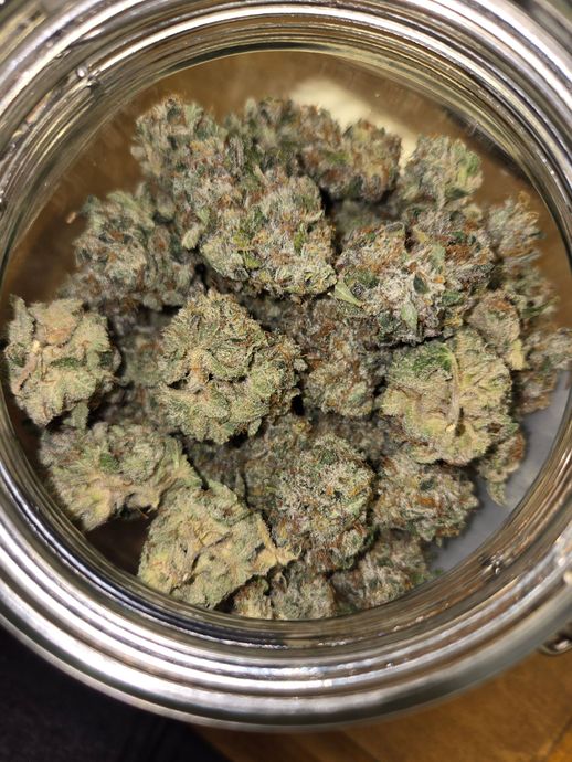 Jar filled with dense, green and purple cannabis buds, covered in trichomes.
