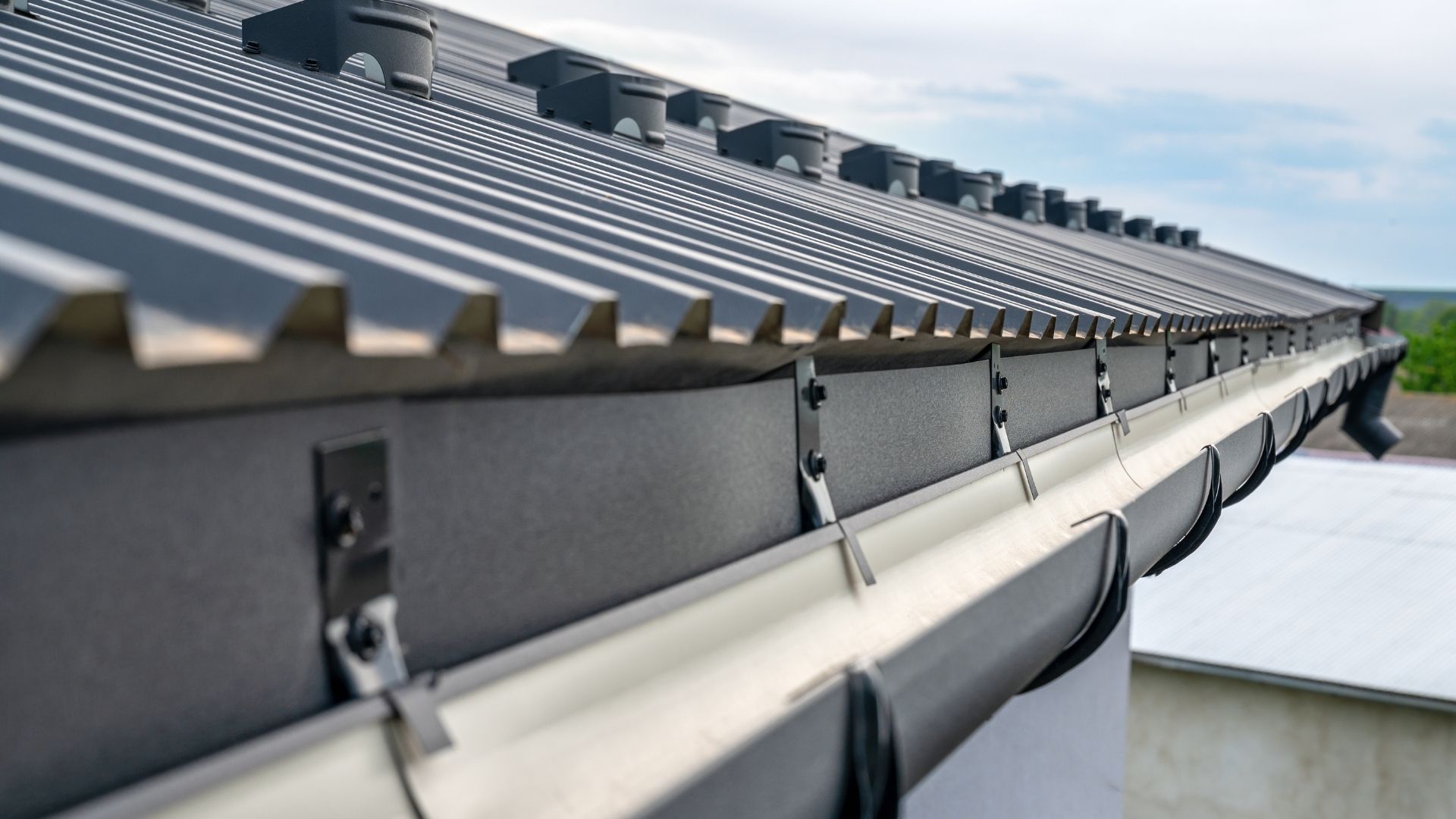 Close-up of a dark metal roof with a matching gutter. Gray sky in background.