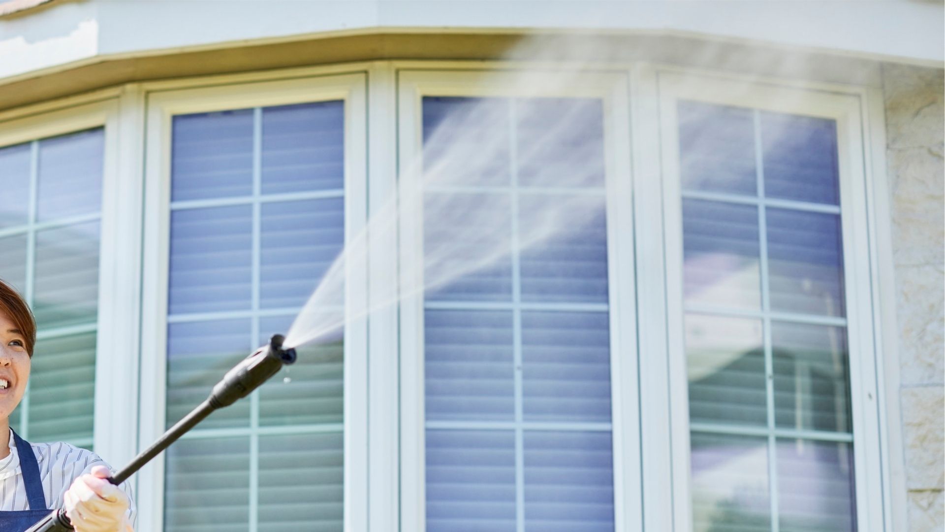 Person spraying water from a pressure washer onto a window.