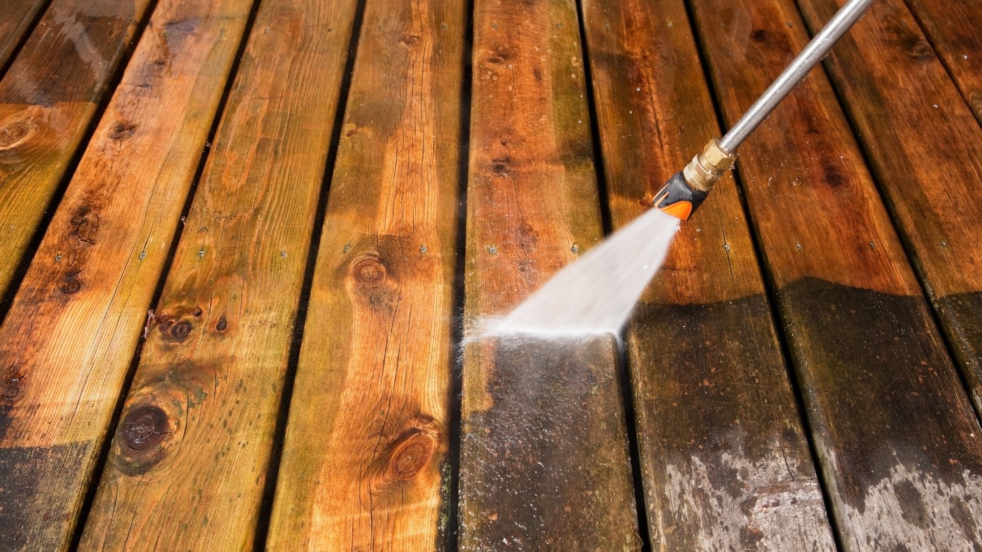Pressure washer cleaning wooden deck, removing dirt and revealing fresh wood.