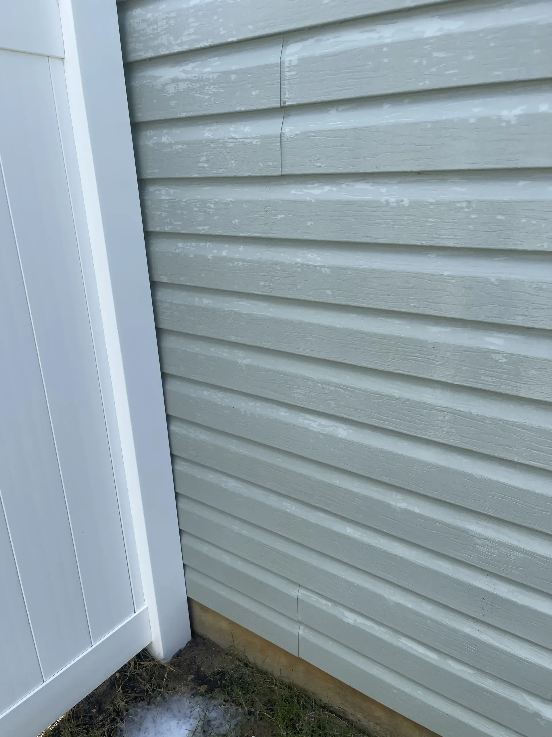 Light gray siding on a building, next to a white fence.