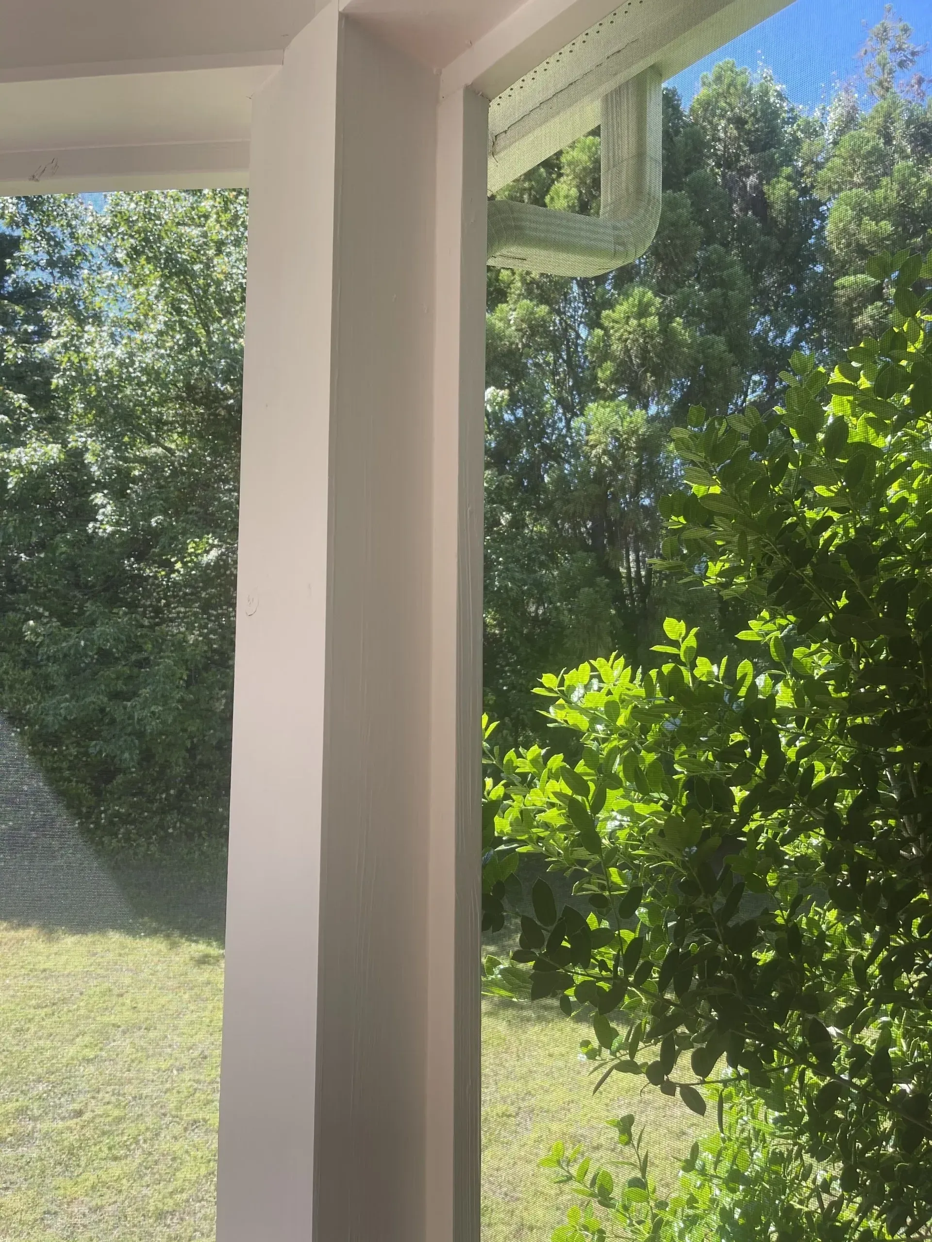 White pillar on a porch with a view of trees and a green lawn.