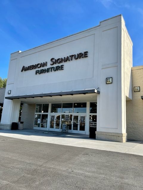 American Signature Furniture store exterior at night. Off-white building with lit entry, black awning, and dark parking lot.