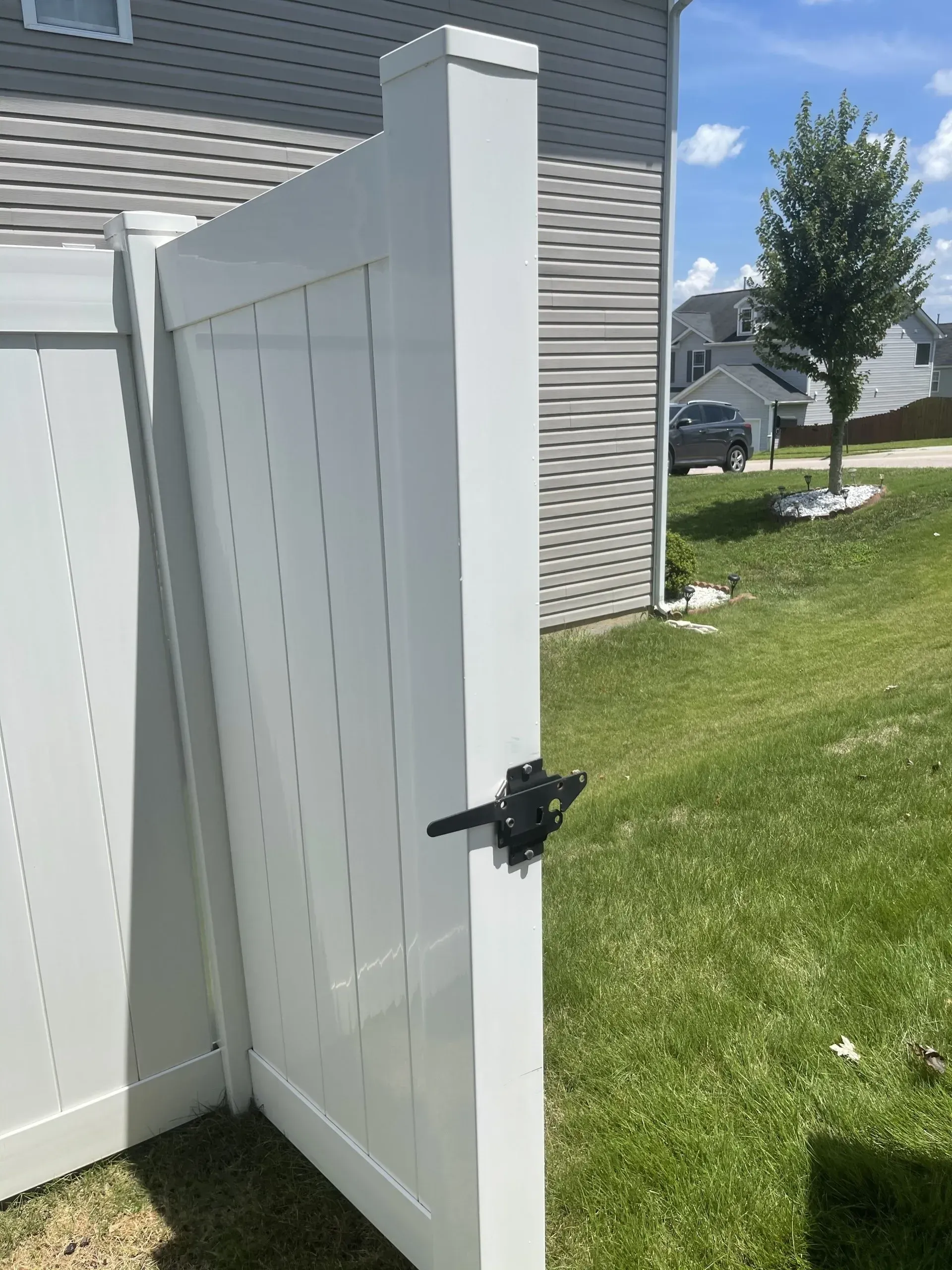 White vinyl gate open in a grassy yard, attached to a white fence, sunny day.