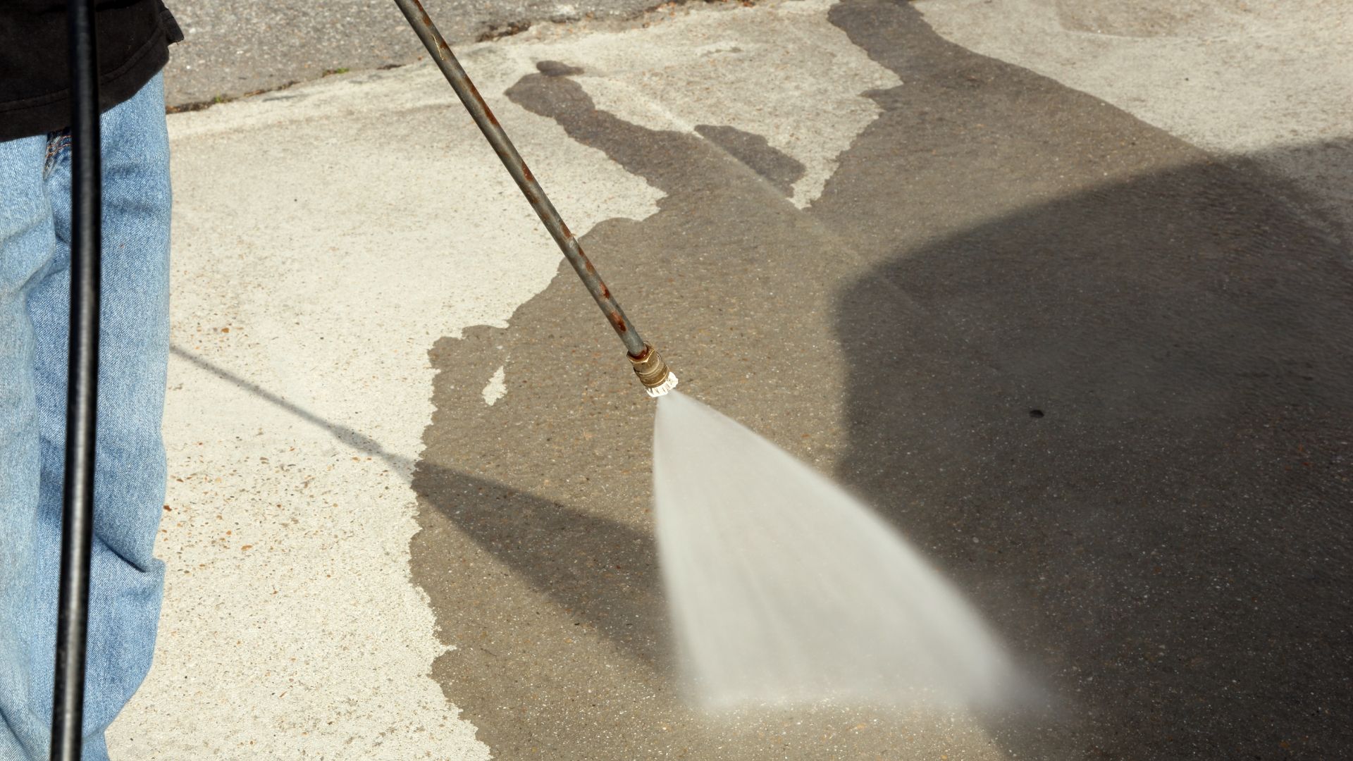 Person power washing a concrete surface with water spray.
