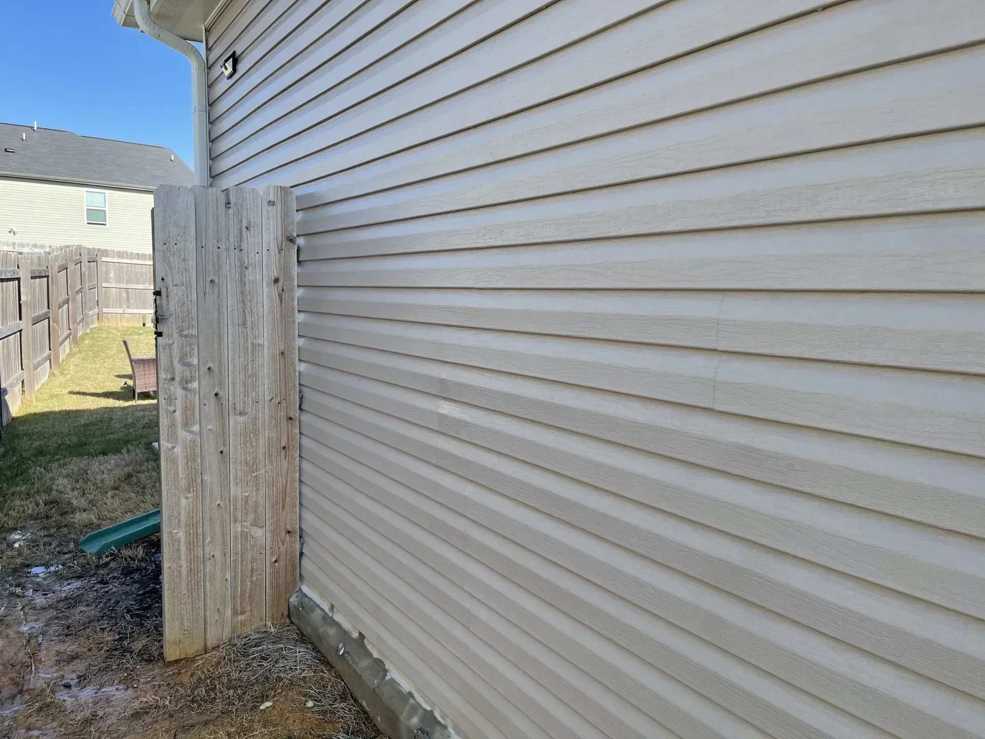 Beige vinyl siding on a house next to weathered wooden fence, outdoors.