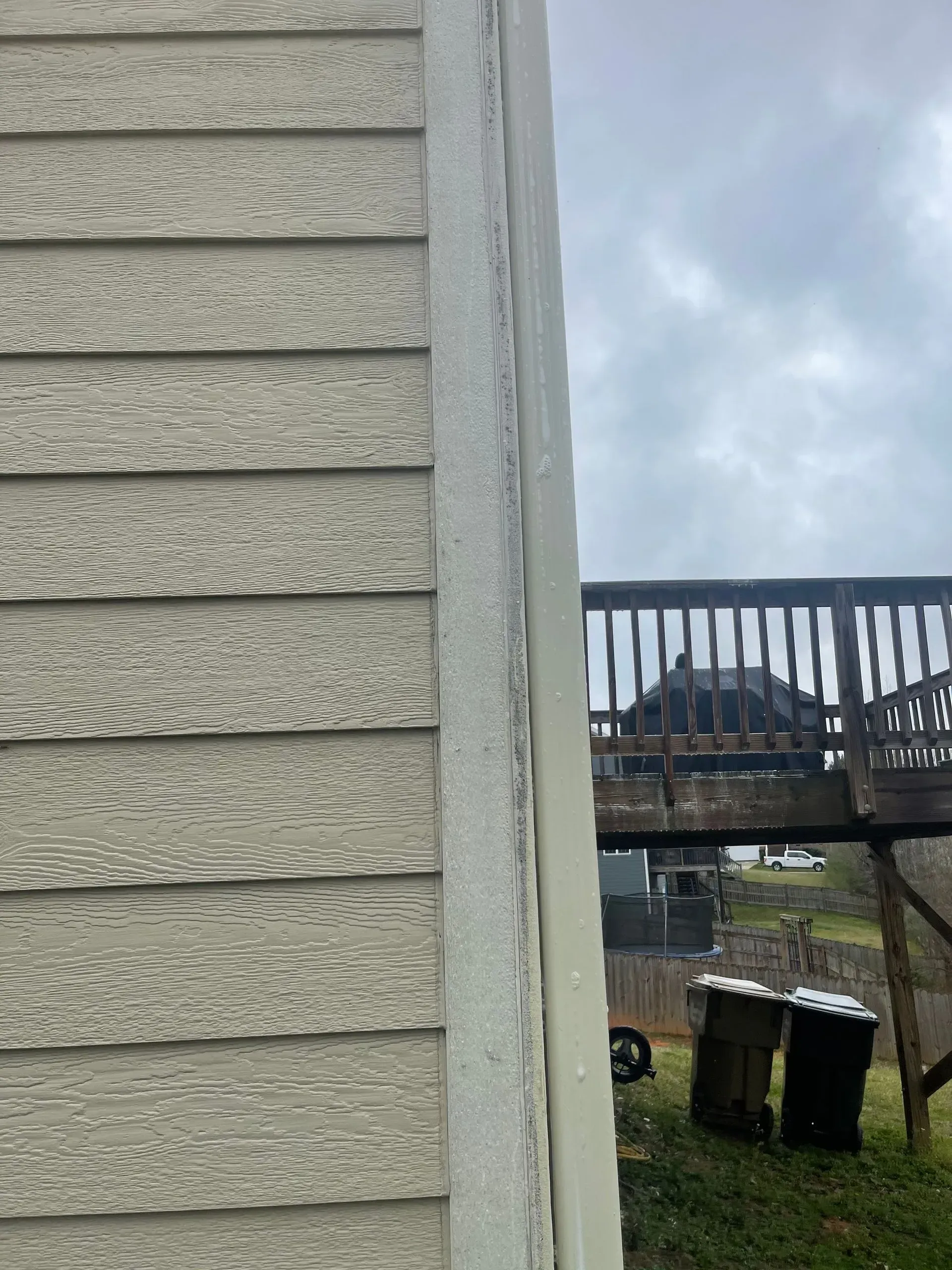 Exterior house siding and trim with a deck in the background under a cloudy sky.