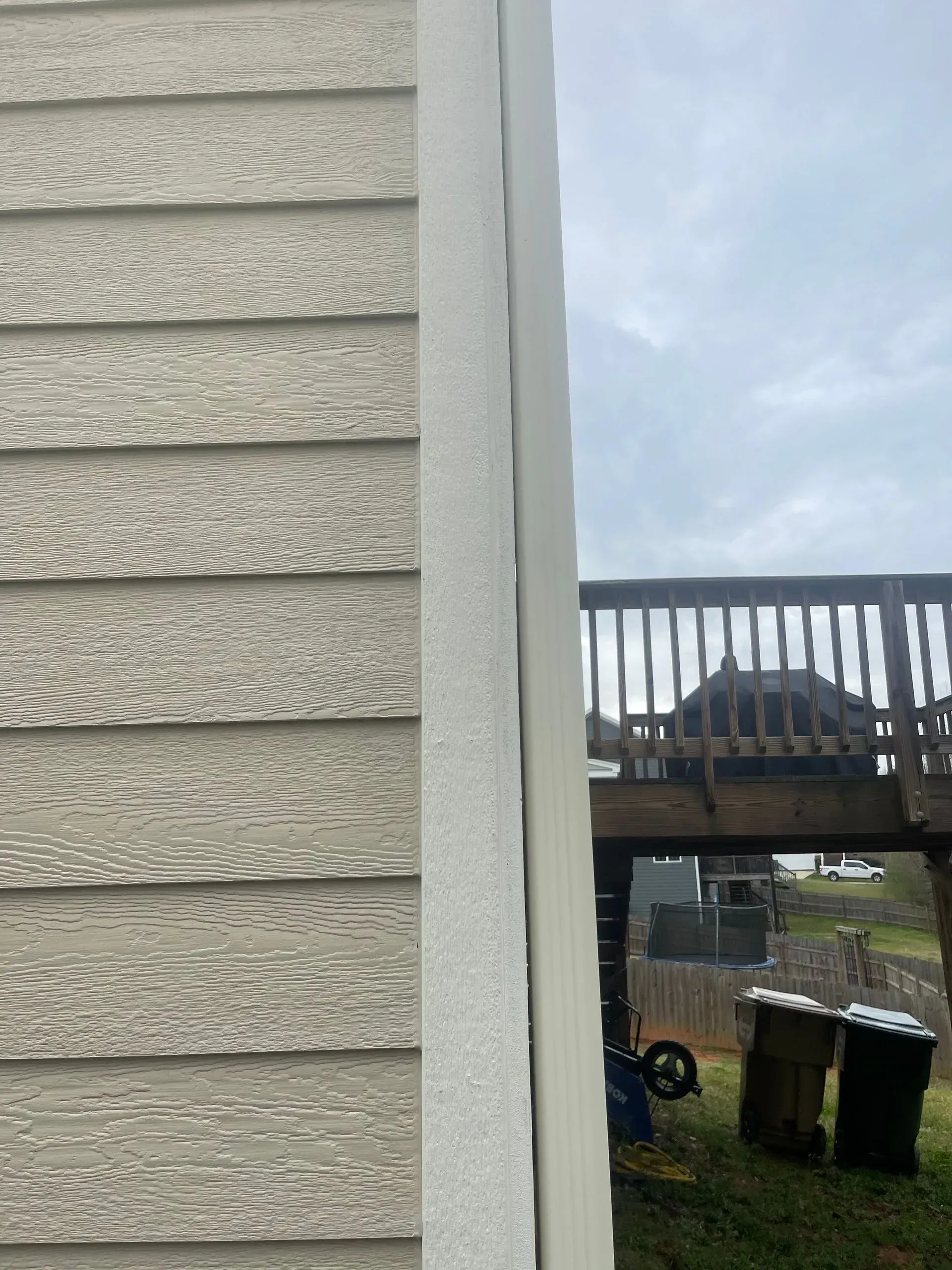 Siding of a house and adjacent painted wall. A deck and sky are visible in the background.