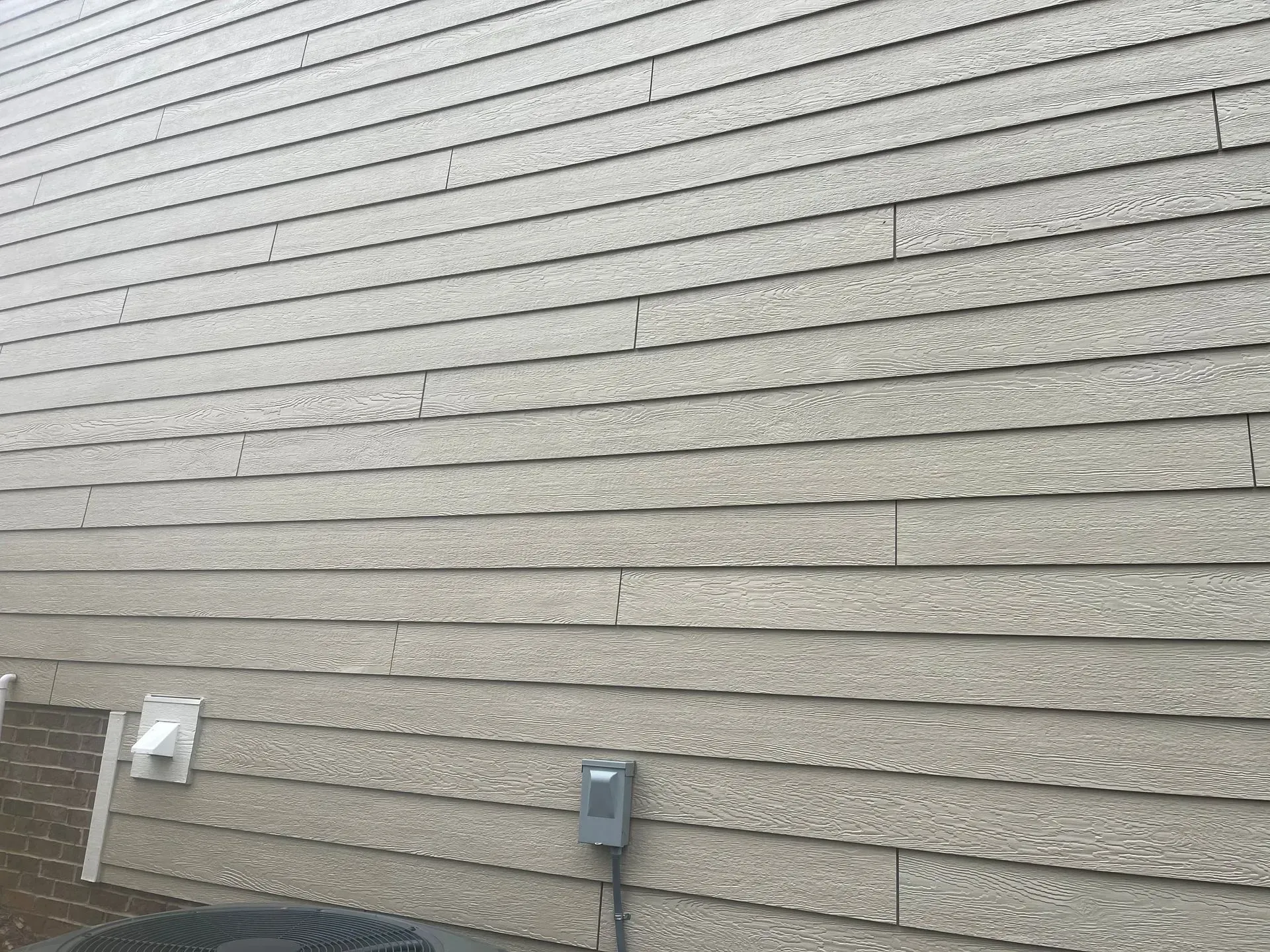 Tan siding on a building with visible horizontal rows and a few small cracks.
