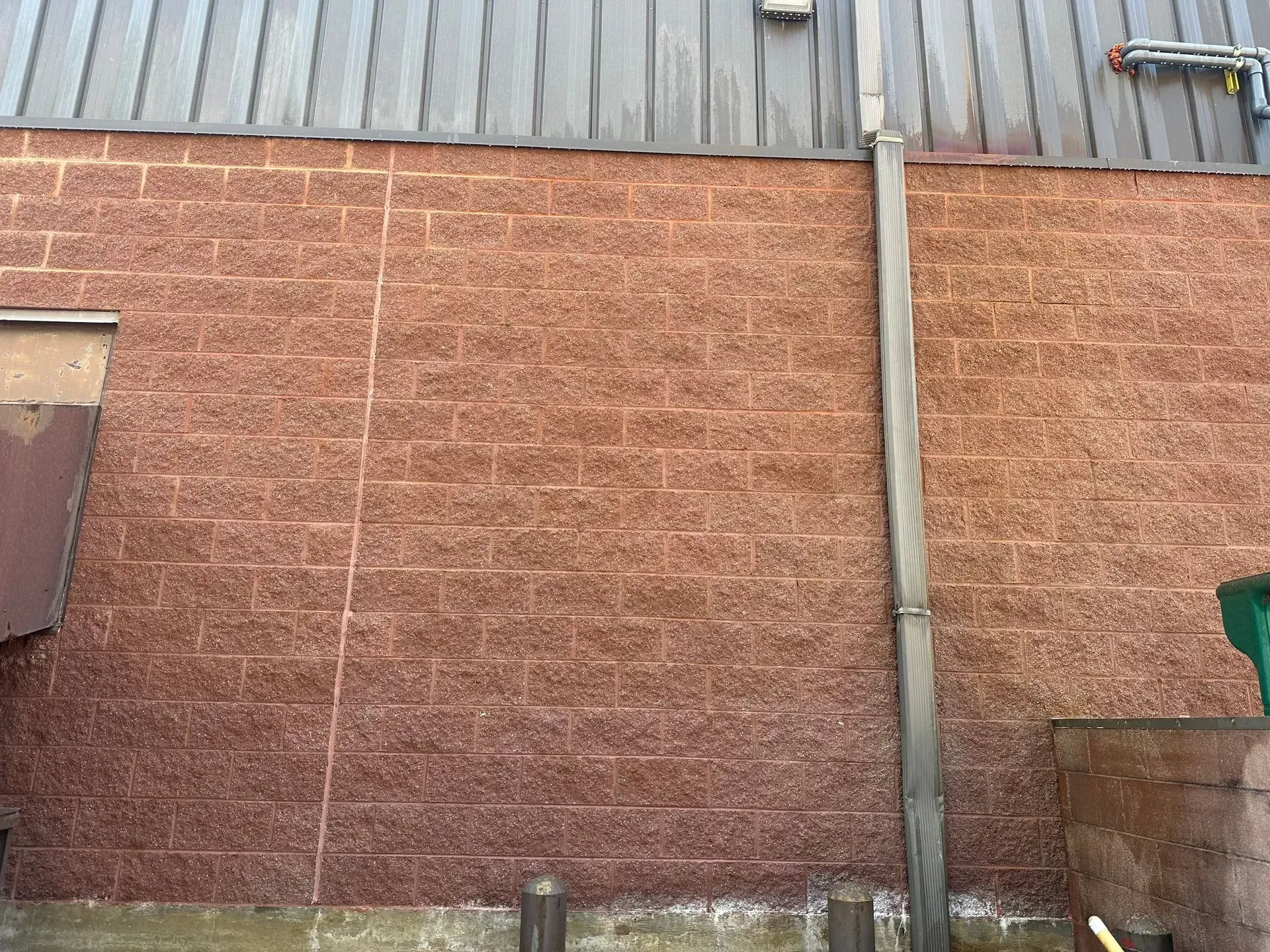 Red brick wall with metal siding, gutter, and a concrete base.