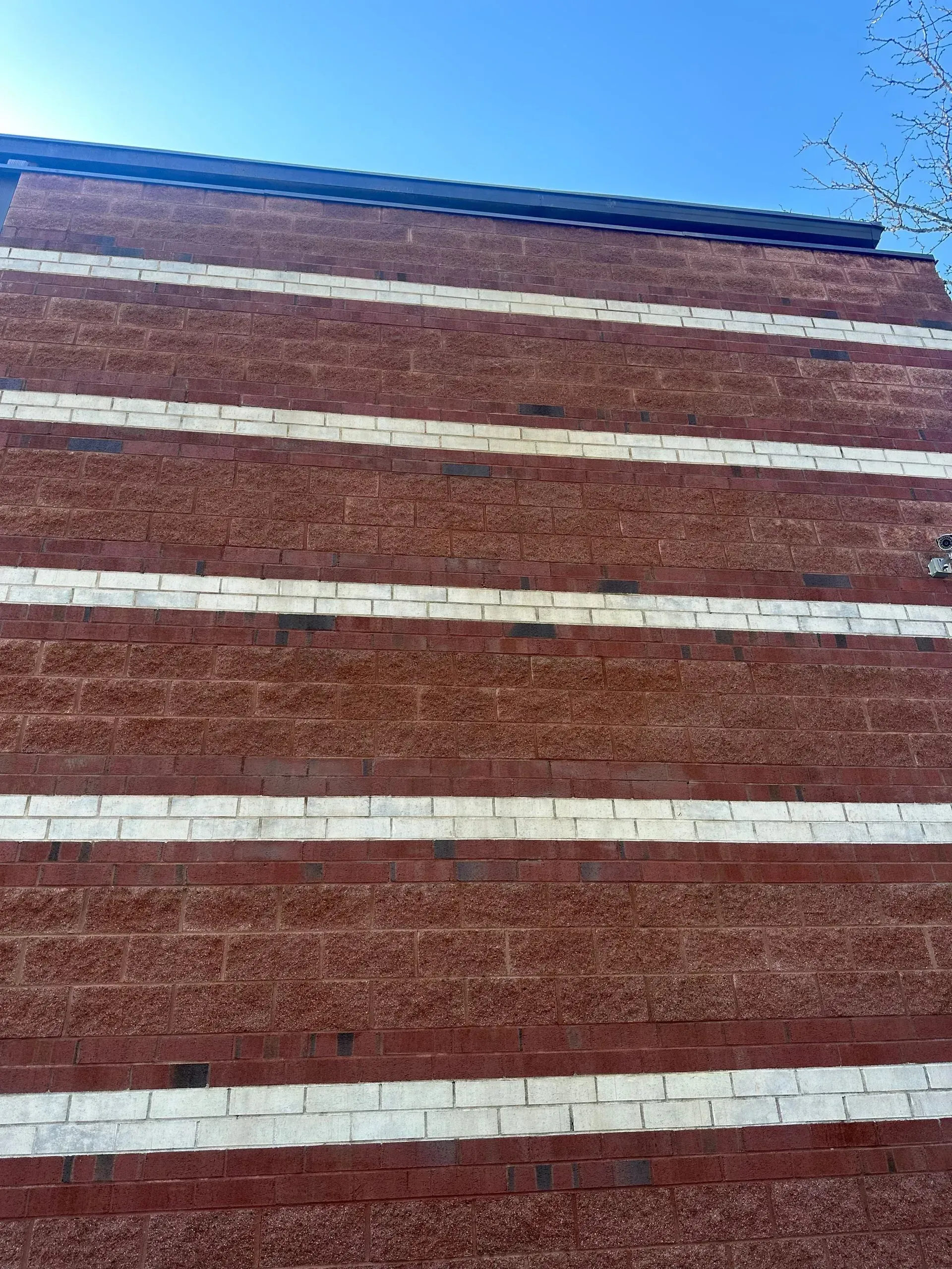 Brick building facade with horizontal white stripes against a clear blue sky.