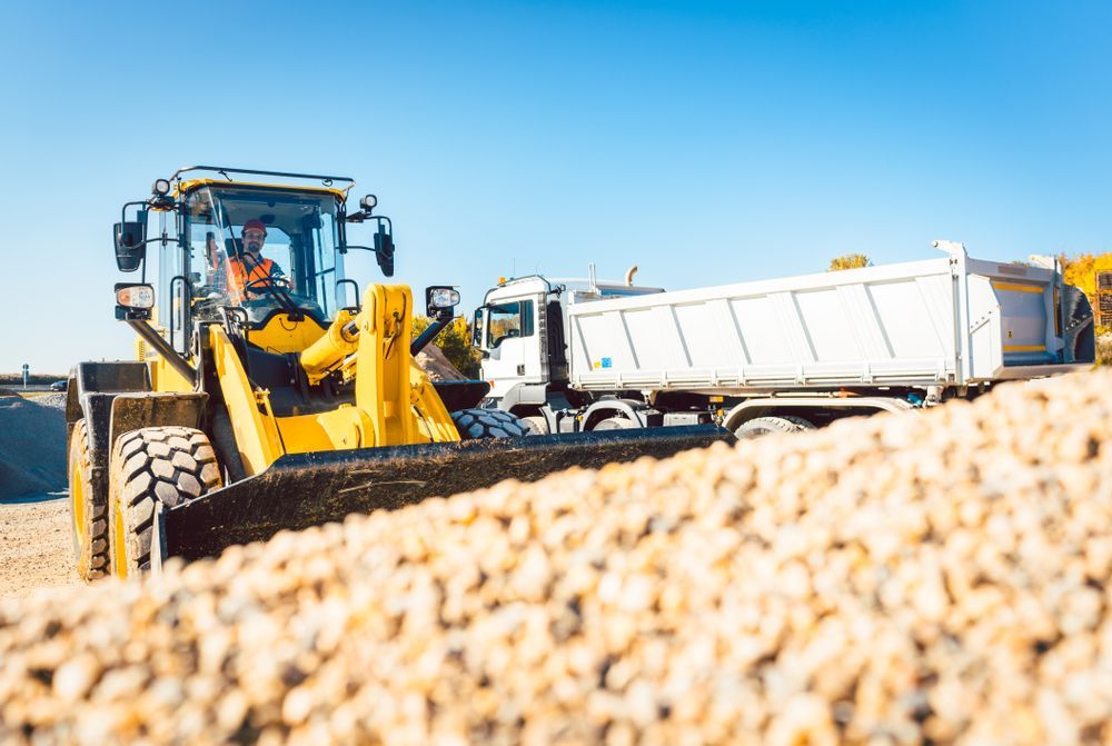 A Bulldozer is Loading a Dump Truck With Gravel on a Construction Site — Hoges Plumbing In Helensburgh, NSW