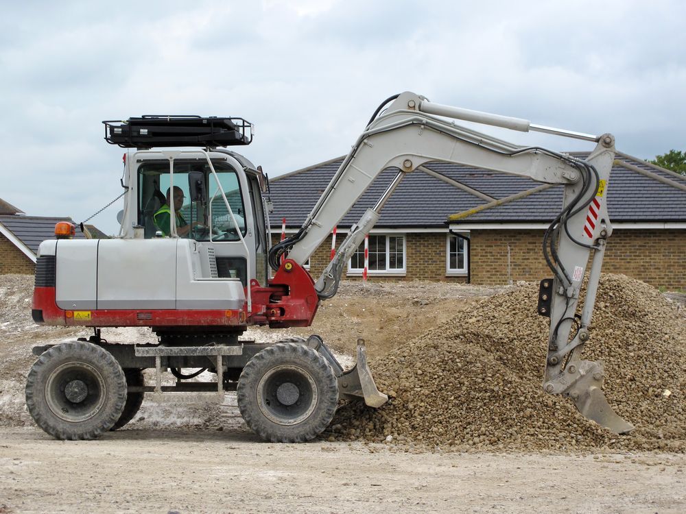 A White and Red Excavator is Sitting in Front of a Pile of Dirt — Hoges Plumbing In Helensburgh, NSW