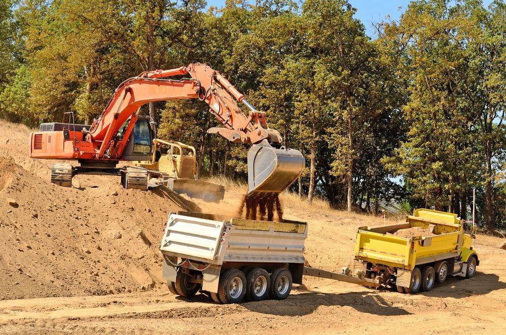 An Excavator is Loading Dirt Into a Dump Truck — Hoges Plumbing In Shellharbour, NSW