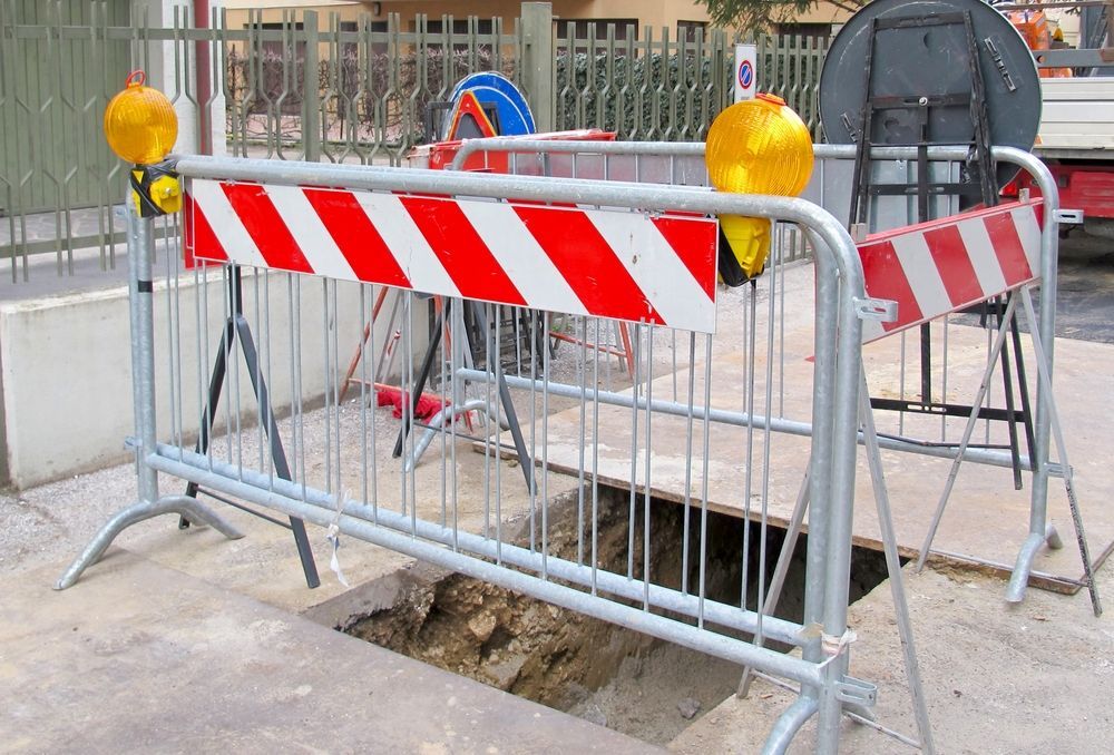 A Red and White Striped Barrier Blocking a Hole in the Ground — Hoges Plumbing In West Wollongong, NSW