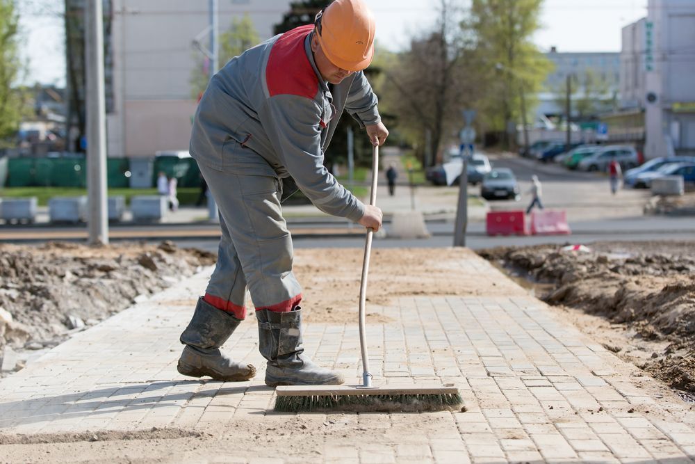 A Man is Sweeping a Sidewalk With a Broom — Hoges Plumbing In West Wollongong, NSW