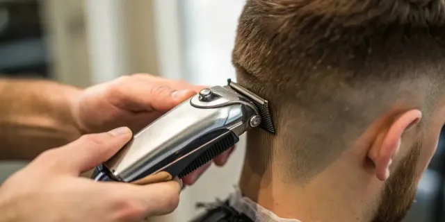 Hands sharpening a knife on a whetstone at a workbench with barber and grooming tools