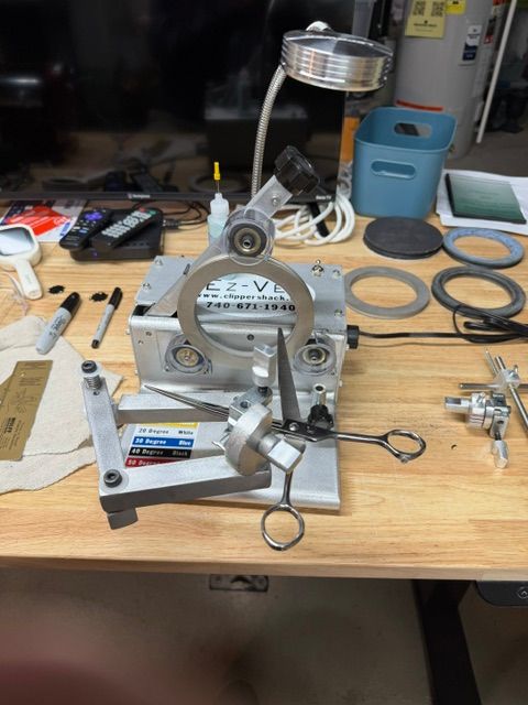 Metal mechanical device on a cluttered workbench with tools and circular parts around it.