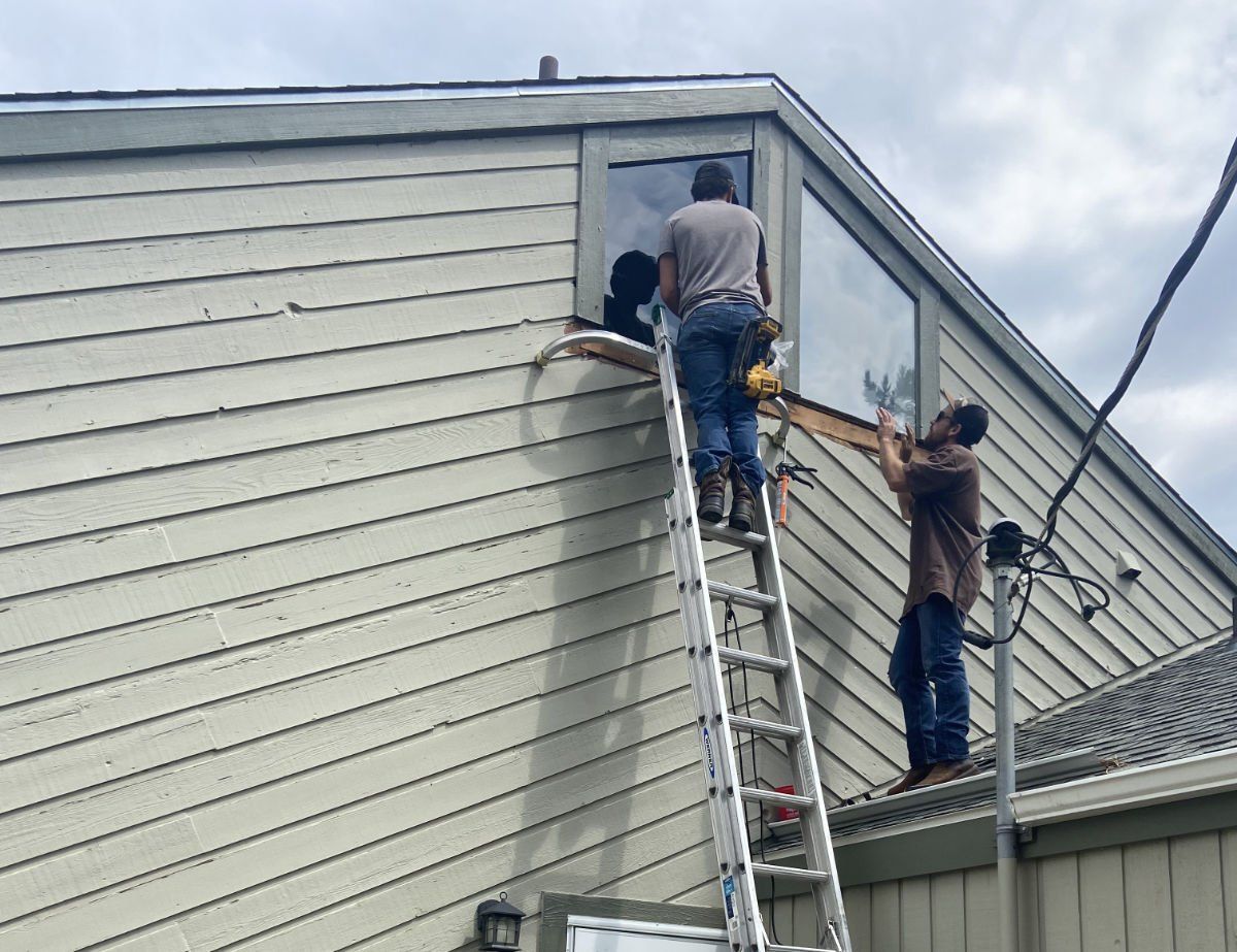 Two men are working on the side of a house with a ladder.