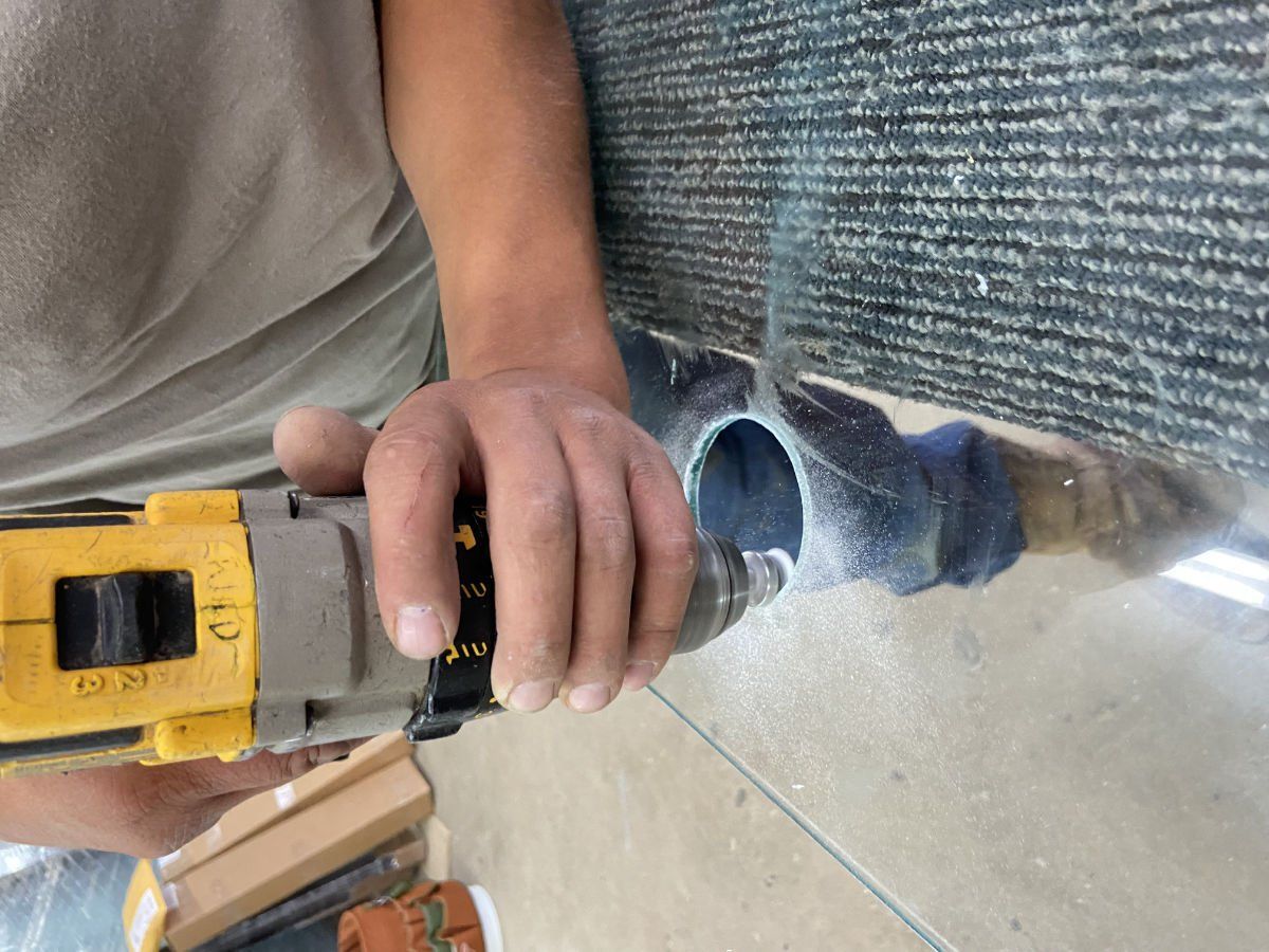 A person is using a drill to cut a hole in a mirror.