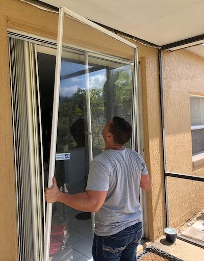 Man installing a sliding screen door on a patio. He holds the frame, looking up.