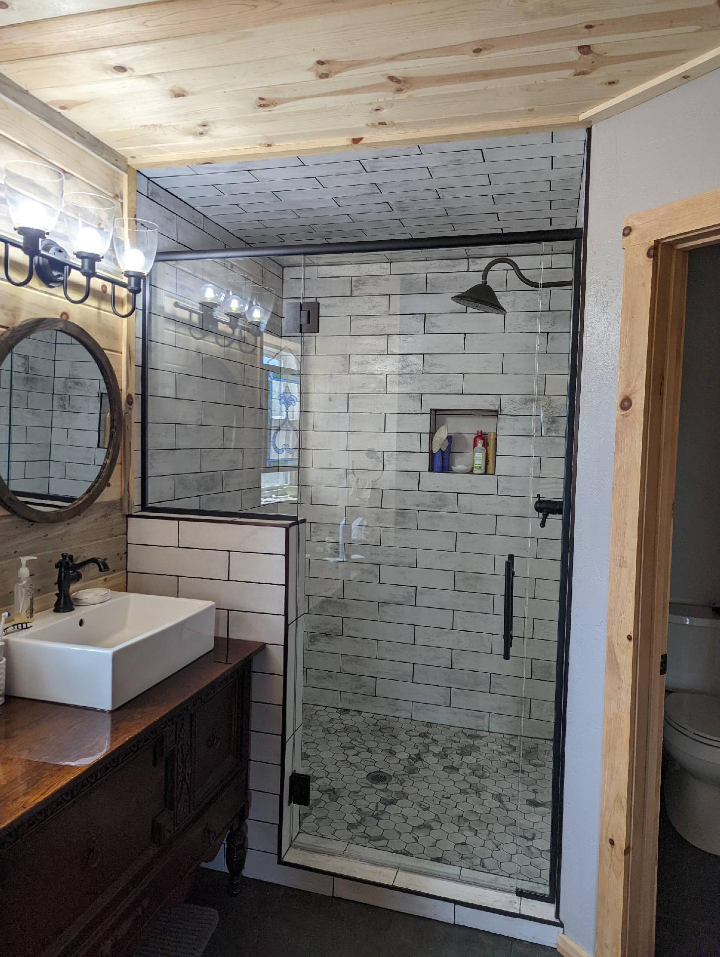 A bathroom with a walk in shower , sink , mirror and toilet.