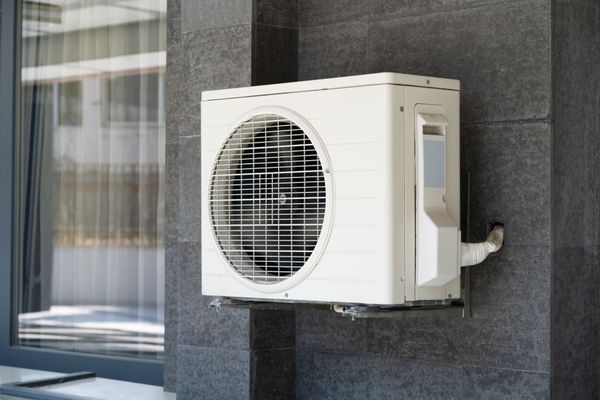White outdoor air conditioner unit mounted on a dark stone wall beside a window